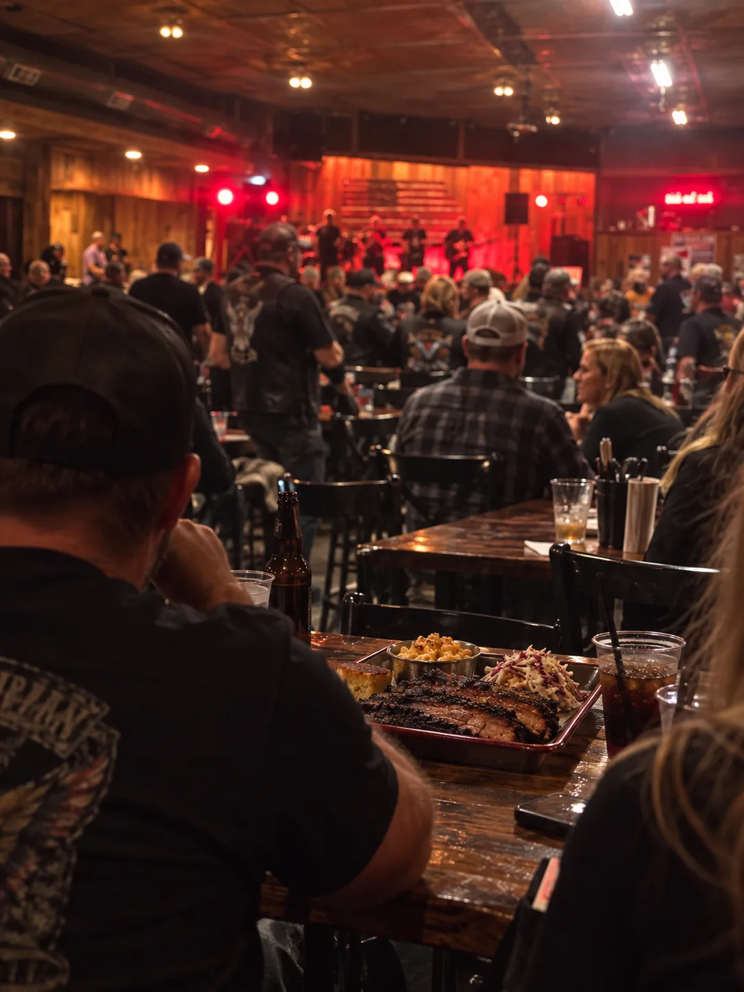 A brisket tray with mac and cheese and slaw on a table at Chrome while a band plays under red stage lights